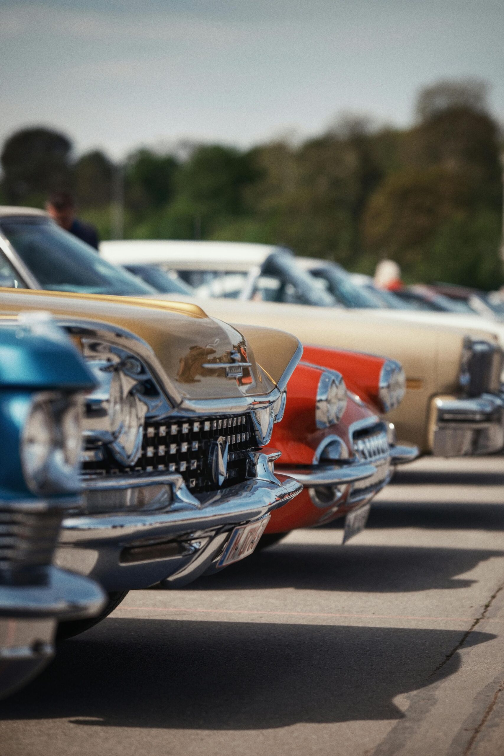 Colorful vintage cars lined up in perfect alignment at an outdoor car show under a clear sky.